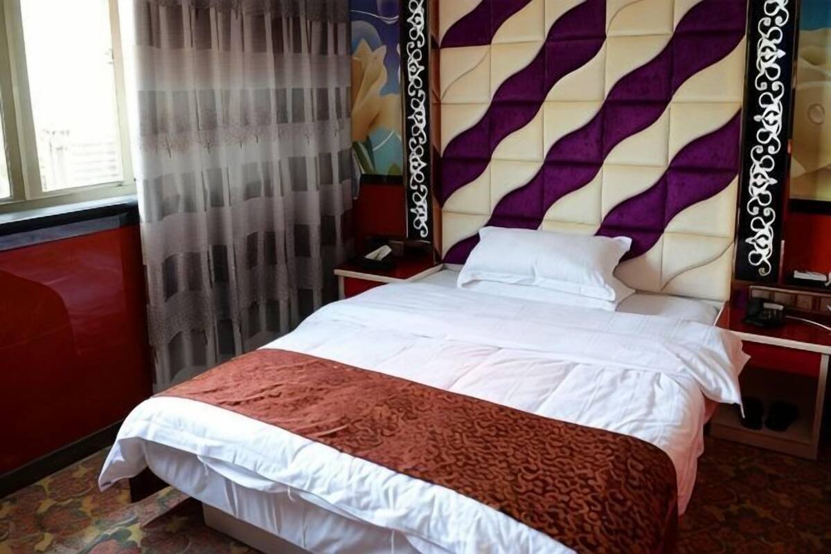 A hotel room with a bed, a nightstand, a red wall, and a window with curtains.