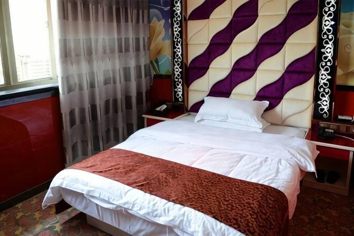 A hotel room with a bed, curtains, a headboard, and a nightstand.