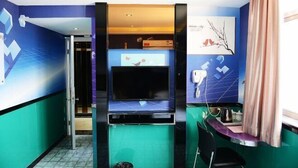 A room with a large flat-screen TV, a small table with a kettle, and a chair. - Yuedi Hotel (Shanghai)