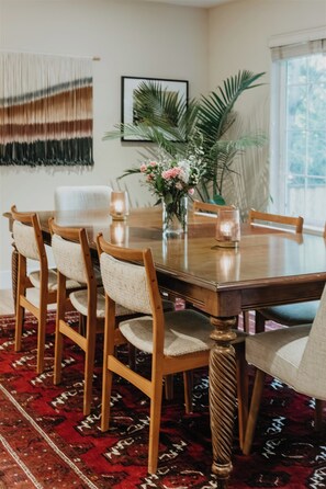 A dining area with a wooden table, chairs, a vase with flowers, and a patterned rug.