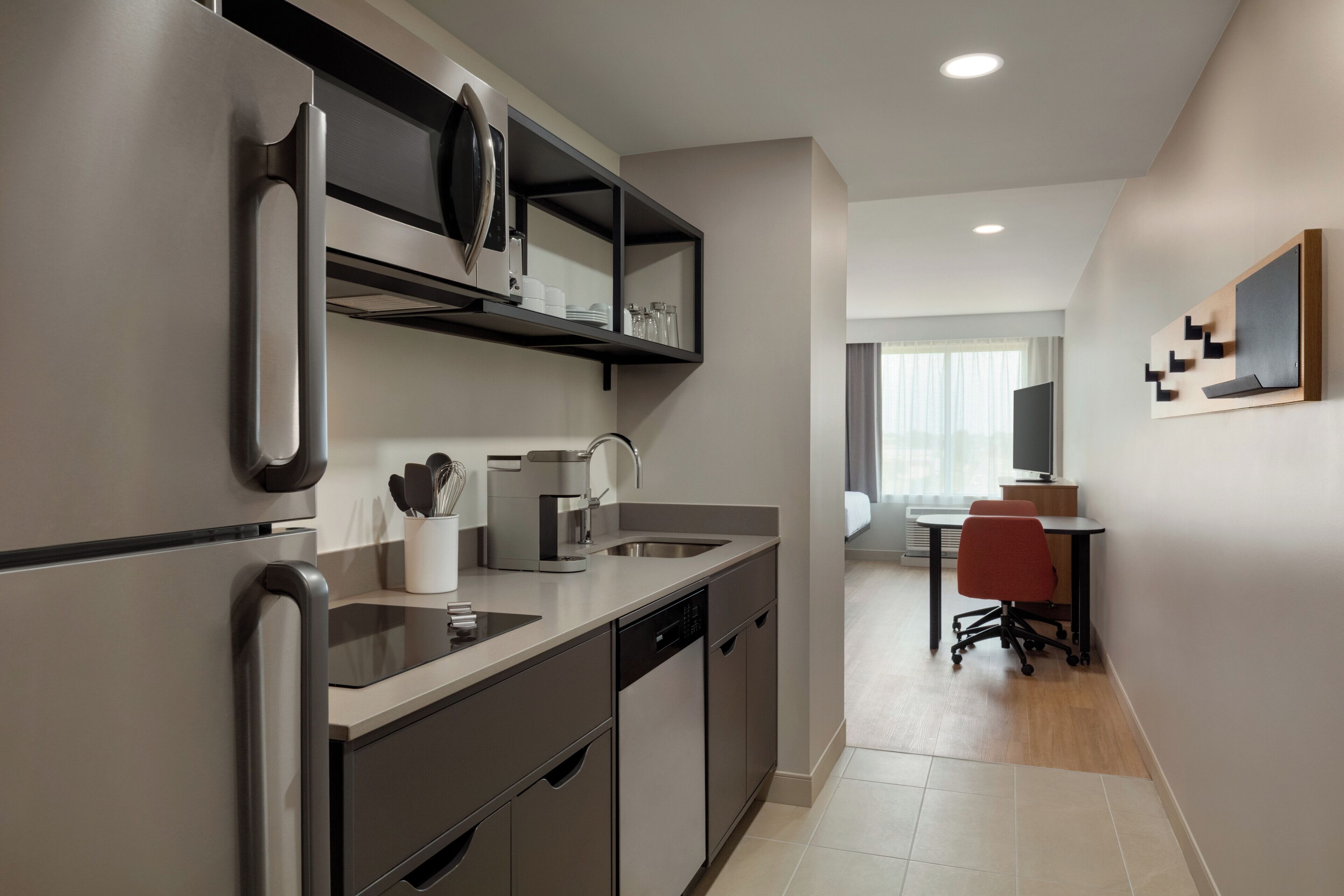 Una cocina moderna con lavavajillas integrado, cafetera y microondas. Se ve un comedor con mesa y sillas al fondo.
