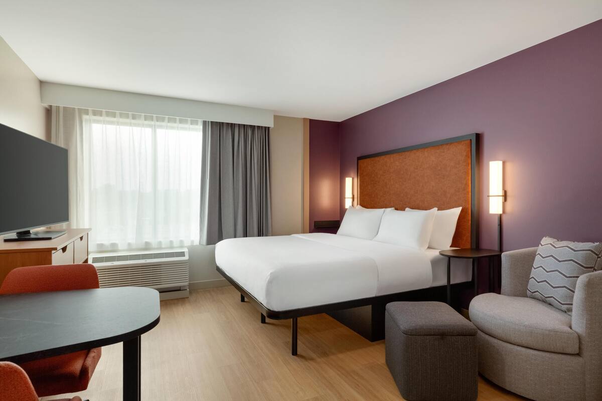Een hotelkamer met een bed, een televisie, een bureau, een stoel, een bank en een lamp.