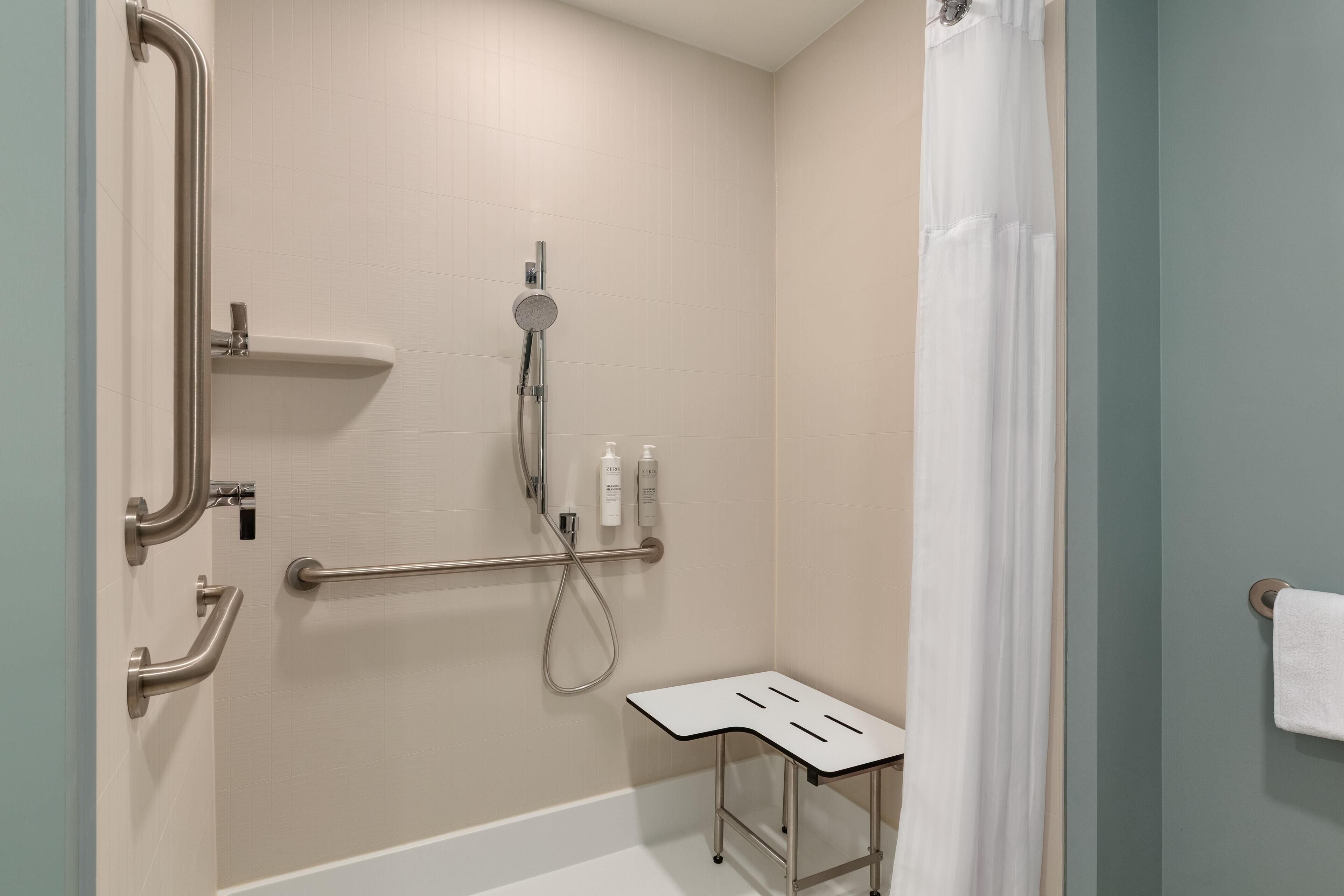 A modern bathroom with a walk-in shower, grab bars, a small table, and a towel rack.