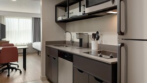 A modern kitchen with stainless steel appliances, a dishwasher, and a coffee maker. There is a dining area with a table and chairs.