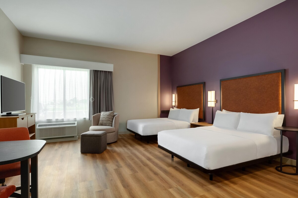 Une chambre d’hôtel avec deux lits, un bureau, une chaise, une télévision et une fenêtre avec des rideaux.