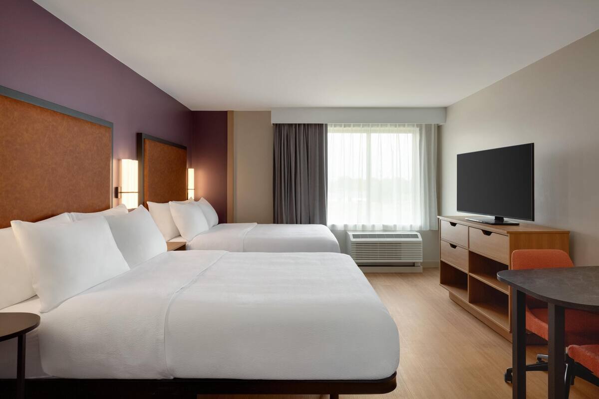 Een hotelkamer met twee bedden, een televisie, een bureau en een stoel.