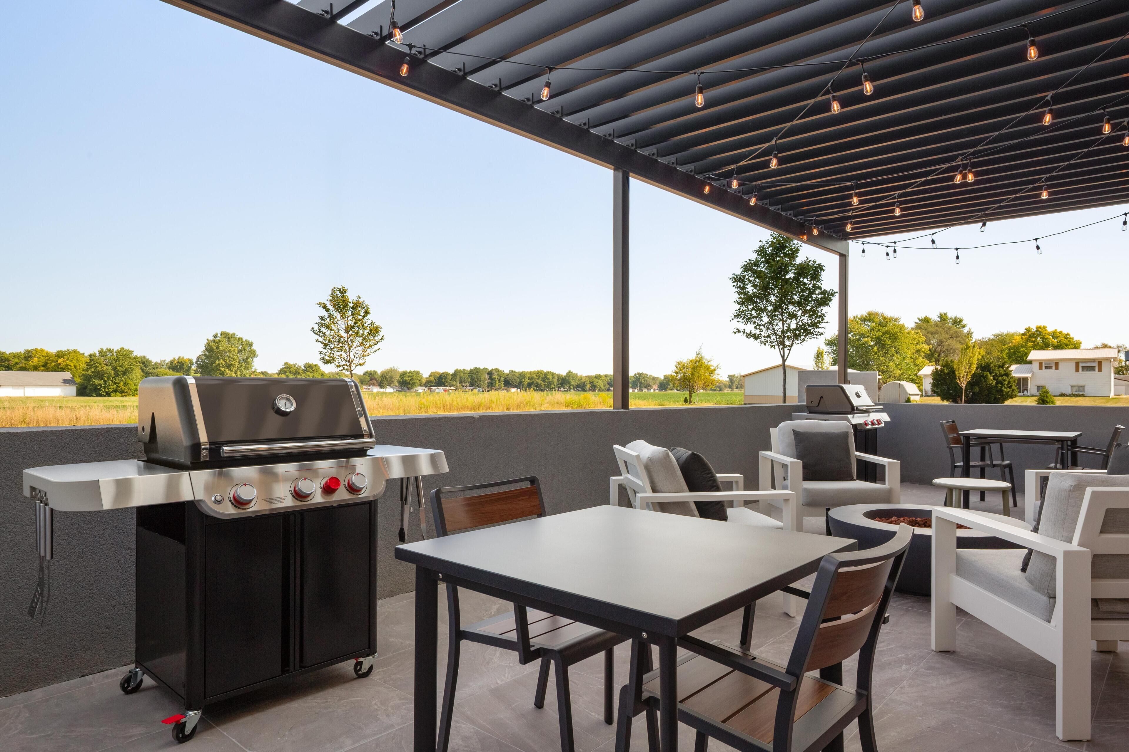 An outdoor patio with a grill, seating, and a pergola with string lights.