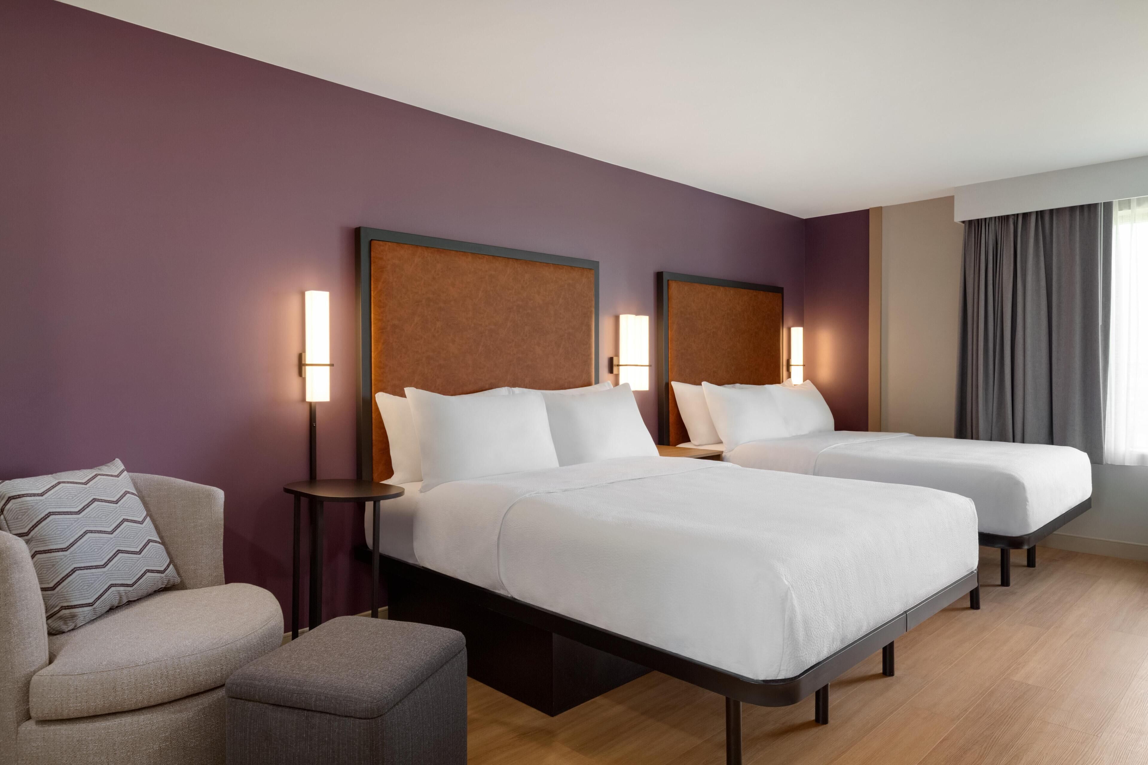A hotel room with two single beds, a sofa, a small table, and a lamp.
