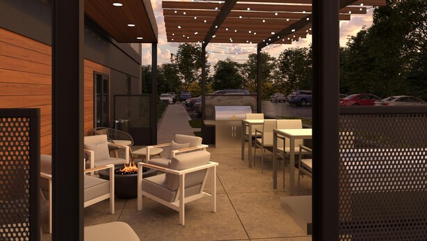 An outdoor patio area with seating and a grill, overlooking a parking lot and trees.