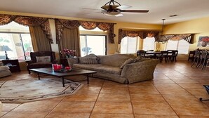 A spacious living room with a large sofa, a coffee table, and a dining area with chairs and a table. - Warm and welcoming Tuscan home in award-Winning Pebble Creek Resort Community. (Goodyear)