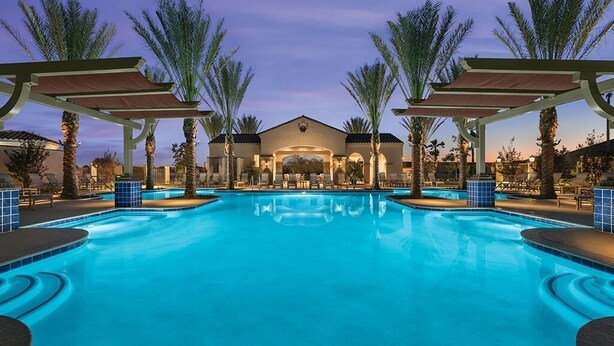 A swimming pool with a covered area, palm trees, and a building in the background. - Warm and welcoming Tuscan home in award-Winning Pebble Creek Resort Community. (Goodyear)