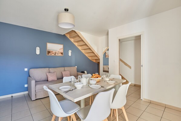Un comedor moderno con una escalera de madera, una pared de acento azul y un sofá con un cojín estampado.
