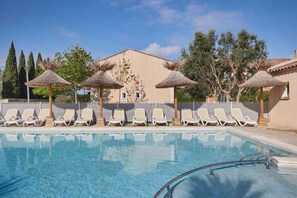 Una piscina con sillas de descanso y sombrillas de paja.