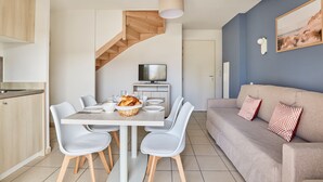 A modern kitchen with a dining area, a staircase, a TV, and a sofa with patterned cushions. - Maisonnette Confortable | Terrace Privée + Parking (Aigues Mortes)