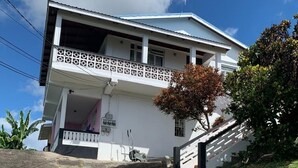 A two-story house with a balcony, a staircase leading to the entrance, and a grassy area.