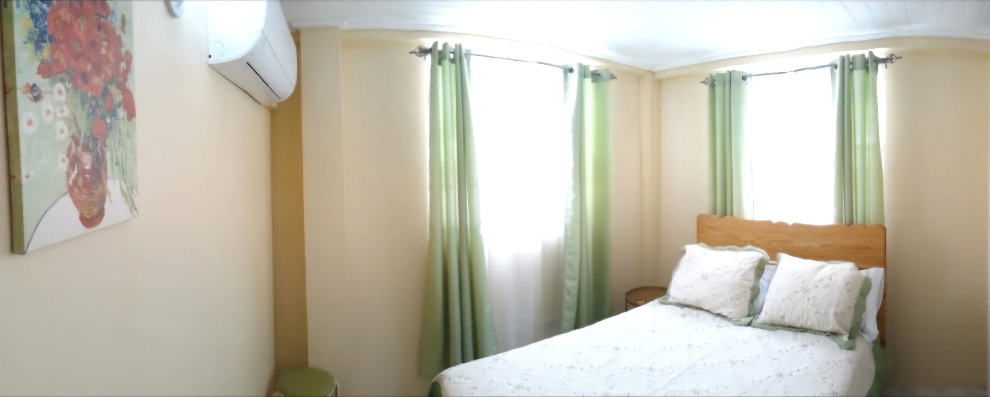 A bedroom with a bed, green curtains, a nightstand, and a wall-mounted air conditioner.