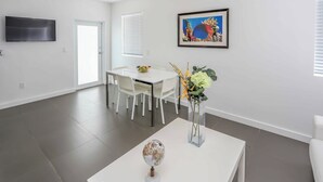 Un salon moderne comprenant un coin repas, un téléviseur à écran plat fixé au mur, une œuvre d’art encadrée et un vase avec des fleurs posé sur une table basse.