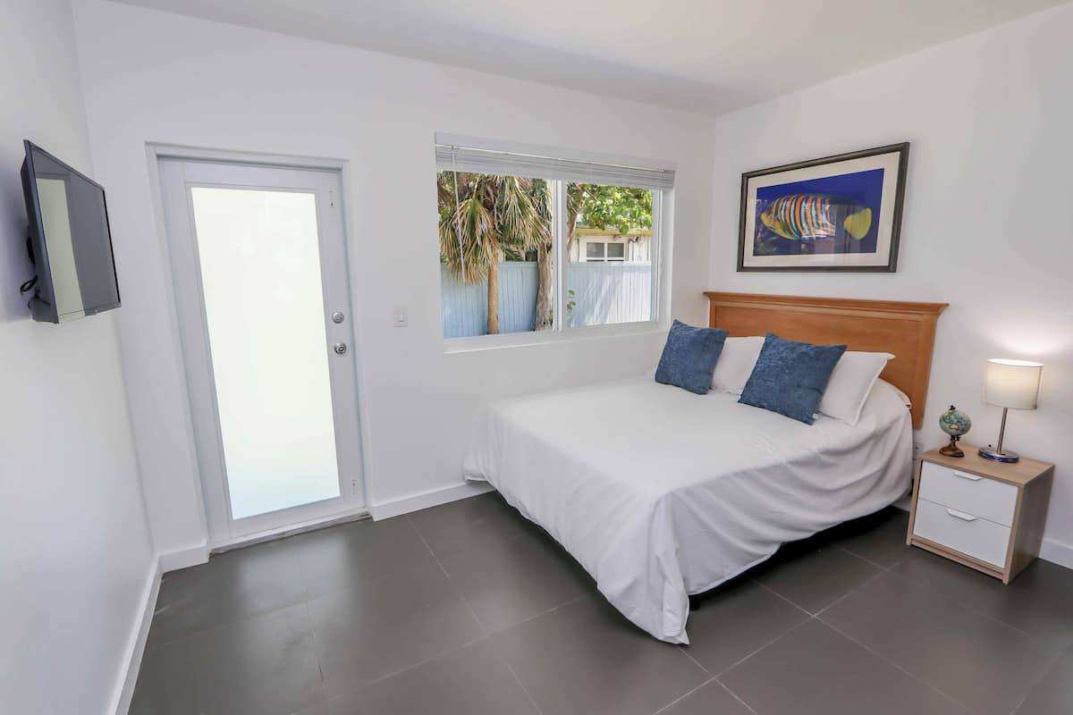 A bedroom with a bed, a nightstand, a TV, a window, and a door.