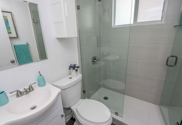 A bathroom with a white sink, toilet, and glass-enclosed shower. - Mimo Bungalows By Renzzi (Miami)