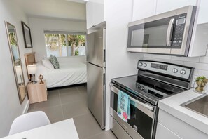 A compact kitchen with a refrigerator, microwave, oven, and a small dining area. - Mimo Bungalows By Renzzi (Miami)