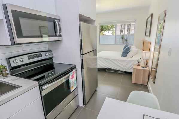 A compact kitchen with a microwave, stove, and refrigerator. A small dining area with a table and chairs is visible. - Mimo Bungalows By Renzzi (Miami)