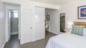 Une chambre d’hôtel comprenant un lit, une table de chevet, une lampe, un tableau encadré et une porte donnant sur une salle de bain.