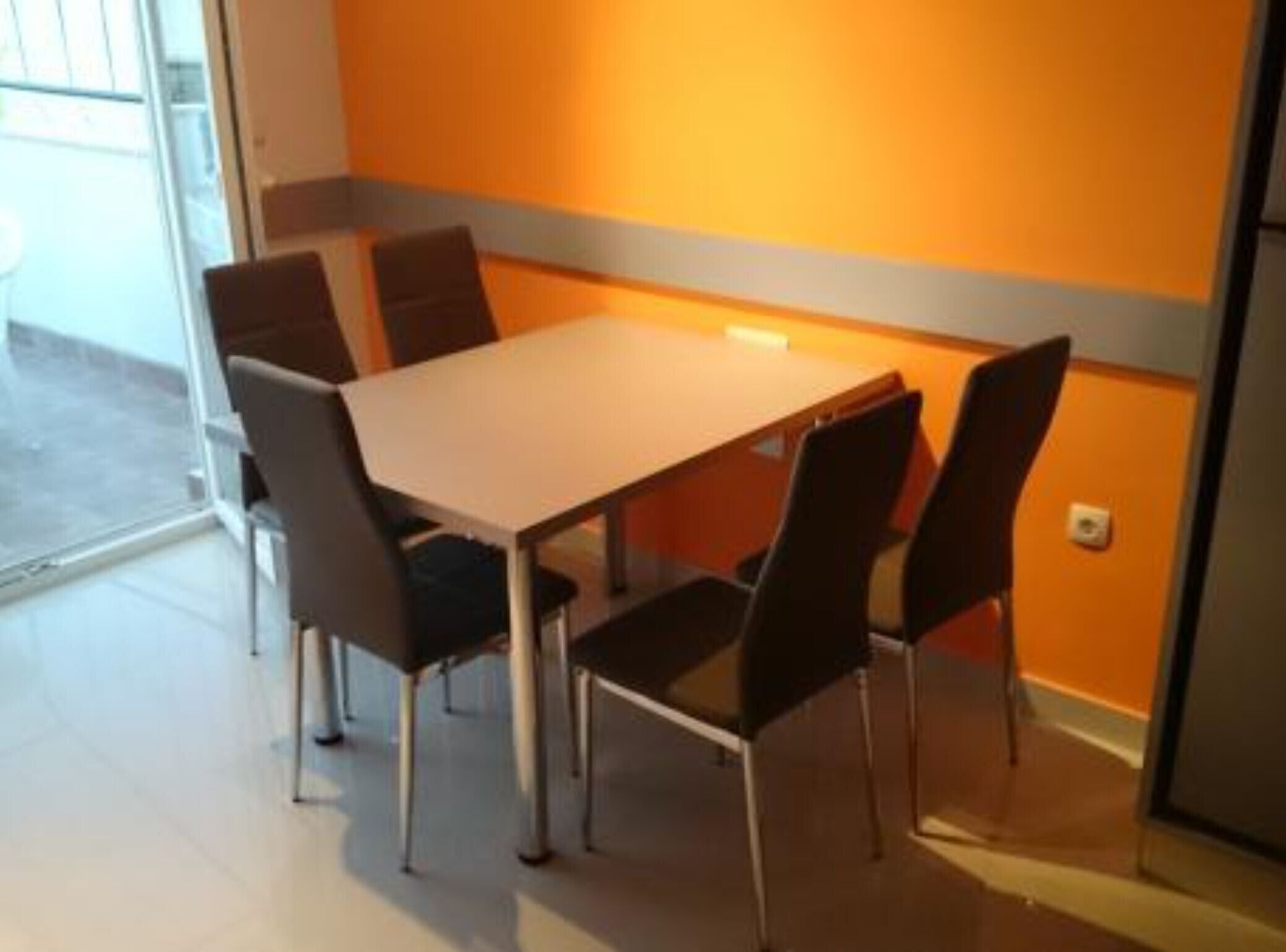 Ein Essbereich mit Tisch, Stühlen, einem Fenster und einer orangefarbenen Wand.