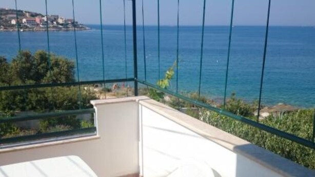A balcony with a view of the sea, a white chair, and a table.