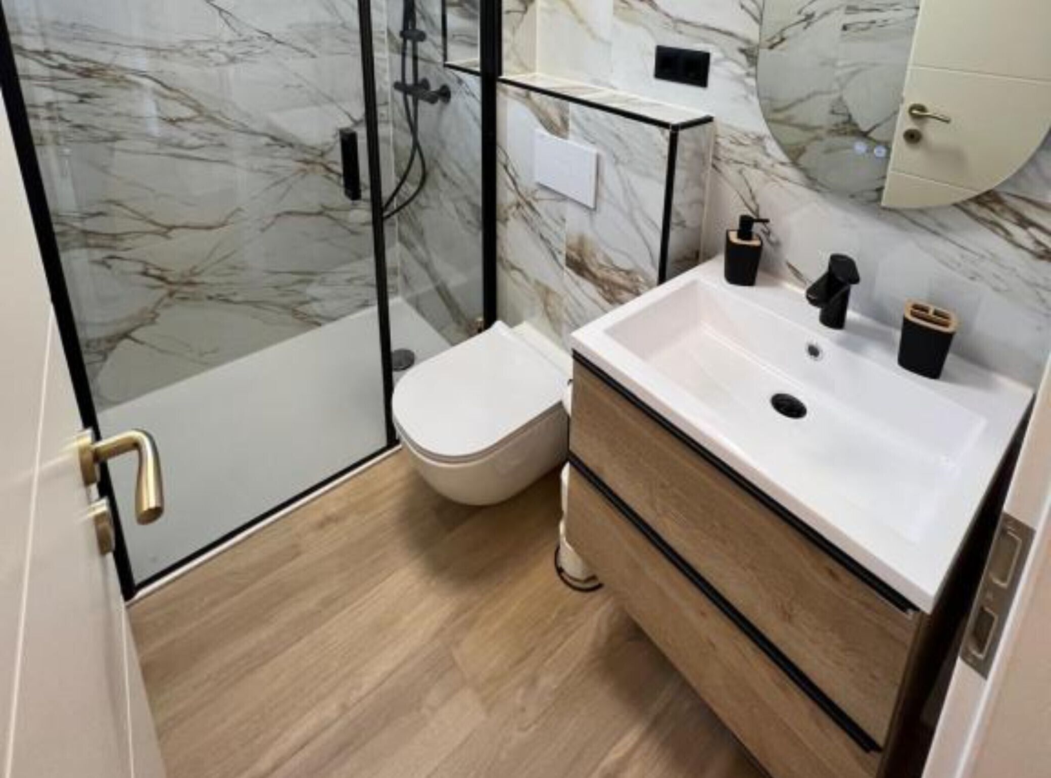 Un baño moderno con cabina de ducha de vidrio, inodoro blanco y tocador de madera con lavabo.