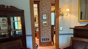 Une pièce comprenant deux fauteuils en cuir, un meuble en bois aux portes vitrées, un lustre et un miroir au mur.