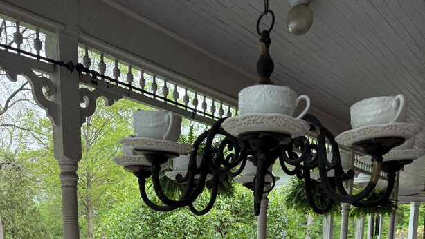 Une véranda couverte avec des balustrades blanches, une chaise en osier et un lustre orné de tasses à thé blanches.