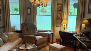Un salon traditionnel comprenant un canapé, un fauteuil, un pouf et un bureau avec une lampe.