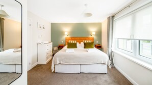 A hotel room with a large bed, two bedside tables, a nightstand, a mirror, a window with curtains, and a headboard with wall-mounted lights. - Cottage in Thirsk With Scenic Trails & Spa (Thirsk)