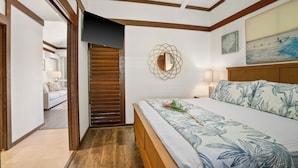 A bedroom with a bed, a ceiling fan, a painting, and a wooden door. - New Renovated April 2025 Charming Apartment In Delightful Kiahuna with AC, (Koloa)