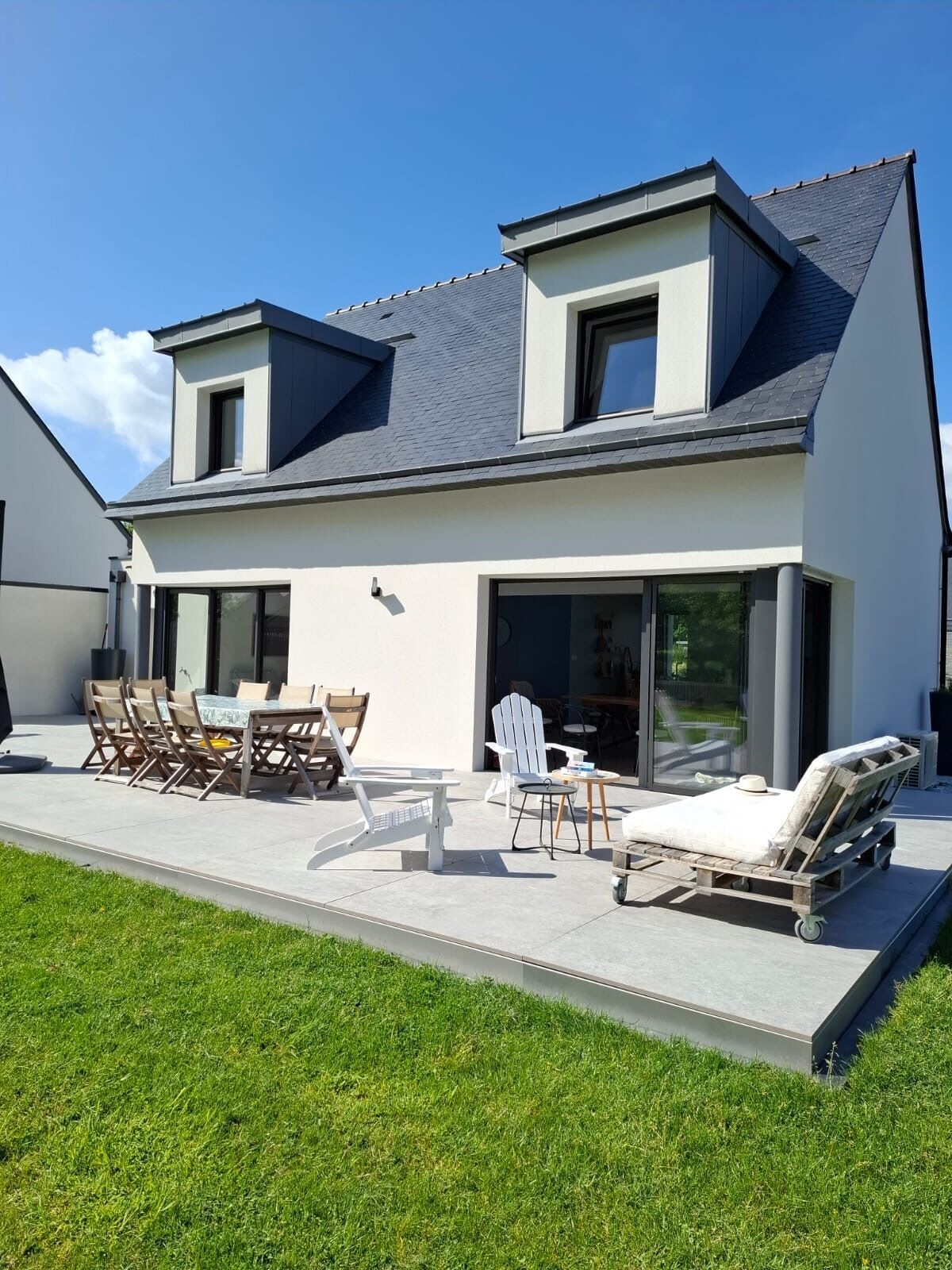 A modern two-story house with a patio area featuring outdoor furniture, including a table and chairs.