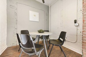 Una habitación con una mesa redonda, cuatro sillas, una obra de arte colgada en la pared y un muro de ladrillos.