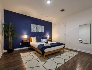 A modern bedroom with a bed, nightstands, a potted plant, and a large mirror.