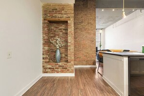 A room with a brick wall, a wooden floor, and a white ceiling.