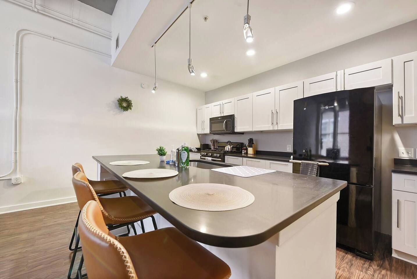 Cozinha moderna com ilha central, eletrodomésticos de aço inoxidável e armários brancos.