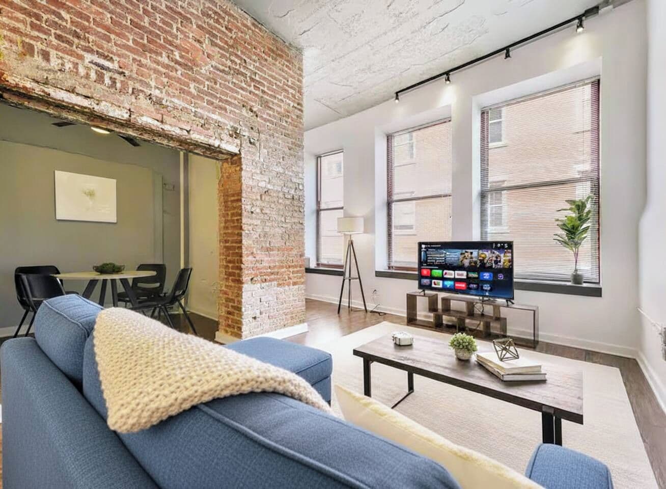 A modern living room with a brick wall, a blue sofa, a coffee table, and a flat-screen TV.