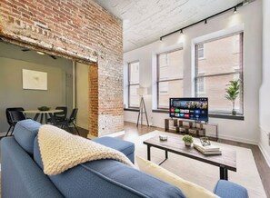 A modern living room with a brick wall, a blue sofa, a coffee table, and a flat-screen TV.