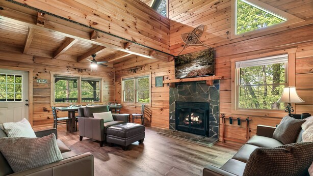 A cozy cabin interior with a stone fireplace, wooden walls, and large windows.