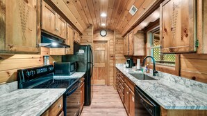 A wooden cabin kitchen with a stove, microwave, refrigerator, sink, and cabinets.