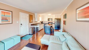 A modern living room with a sofa, a coffee table, and a kitchen area with cabinets and appliances. - Bay-View Escape w/ Private Balcony in Ocean City (Ocean City)