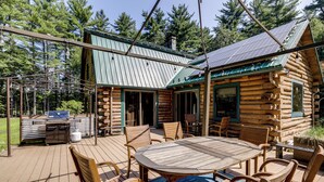 Una cabaña de troncos con terraza, asientos exteriores y una parrilla.