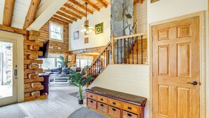 Amplia sala de estar con techo alto, vigas de madera, un pilar de piedra, una escalera y una gran puerta de madera.