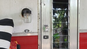Un edificio rojo y blanco con una puerta metálica, una mesita y un tapete estampado.