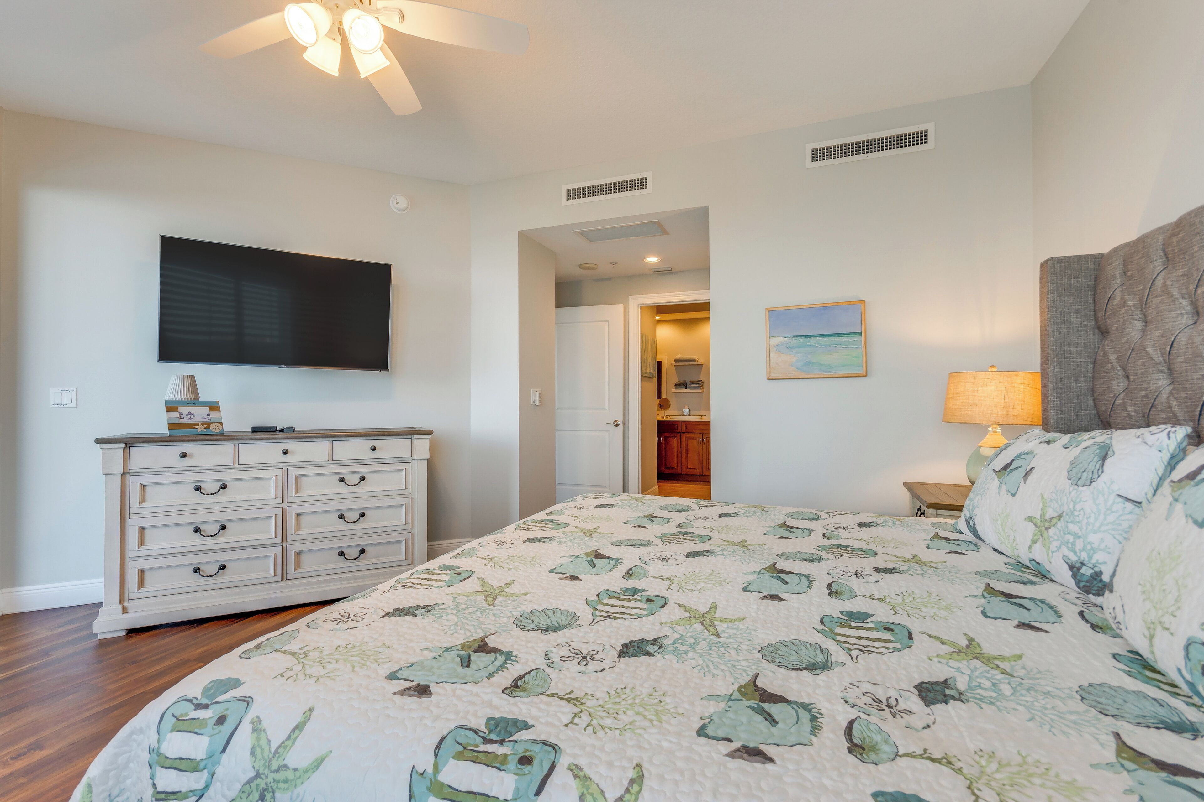 A bedroom with a bed, dresser, TV, and a door leading to another room.