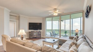 A spacious living room with a sectional sofa, a flat-screen TV, and a balcony with outdoor furniture.