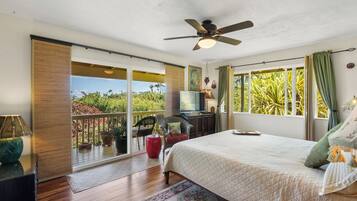 Une chambre avec un lit, un ventilateur de plafond, une télévision et un balcon donnant sur un paysage verdoyant.